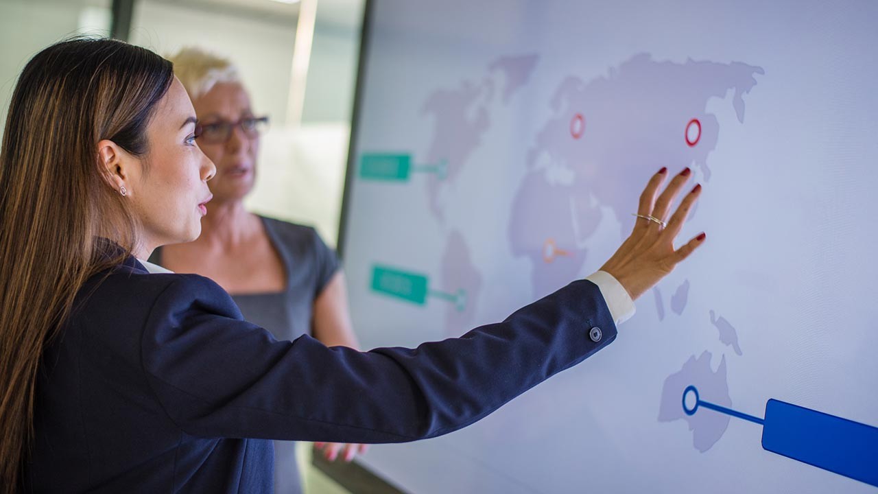 femme d'affaires explique un graphique mondial à un collègue dans une salle de conférence.