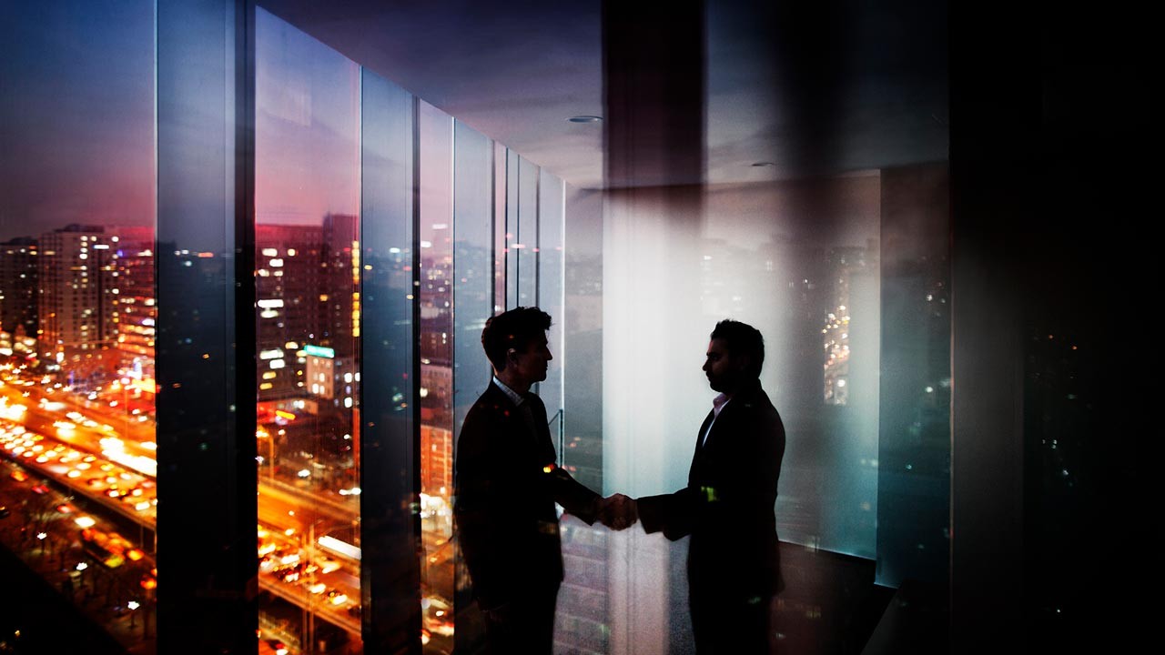 hommes d'affaires se serrant la main dans un bureau la nuit avec vue sur la ville